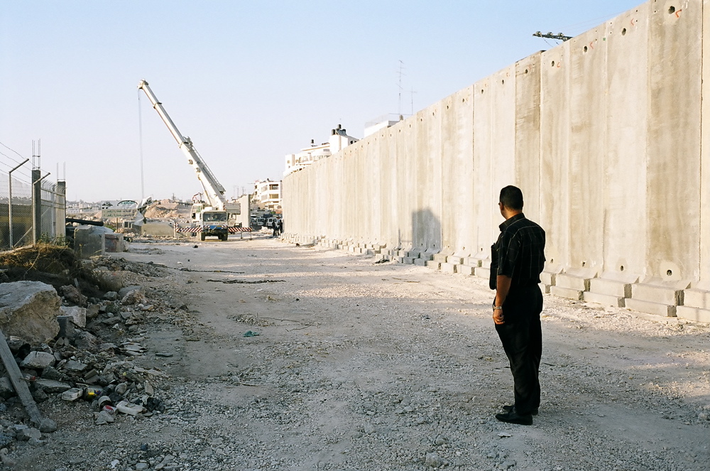 Palestinian man watching as the Barrier concrete block is being pulled up by a crane. September 2004 Ar Ram, Sept. 04, 07