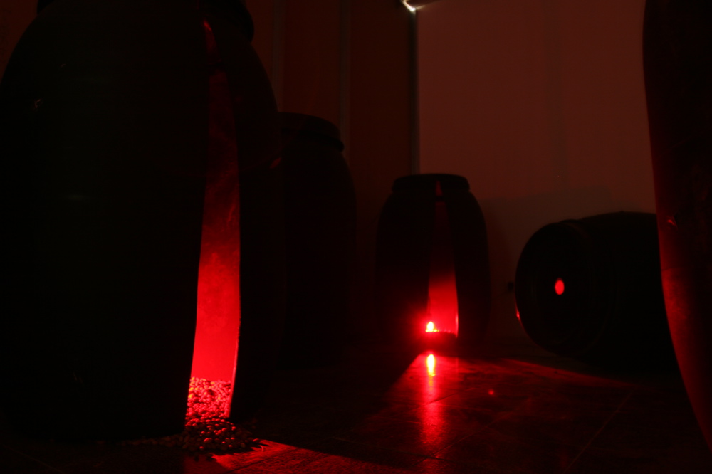 Still Life (2006) black plastic barrels & lids with photographs, black olive pits, red light bulbs & video
Olive Story 09